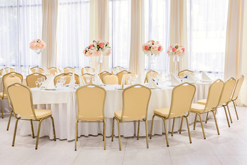 Beautifully decorated room in pastel shades of white with covered tables with flowers in the restaurant for the celebration of the wedding.
