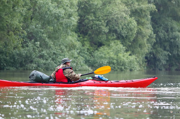 Man in red kayak in red life jacket kayaking in wild Danube river on biosphere reserve in spring