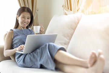 Working woman sitting on the sofa. She is working with a notebook and is drinking coffee. The concept of women working with technology.