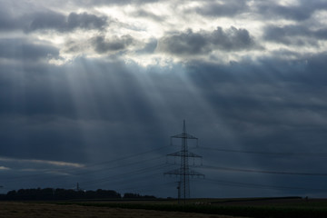 Rays of light making their way through dense clouds. Evening landscape. Agricultural land and power transmission lines.