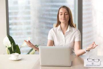 Mindful businesswoman practices breathing exercises at workplace, peaceful woman enjoys yoga with...