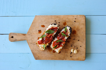 Italian bruschetta with roasted tomatoes, mozzarella cheese and herbs on a cutting board