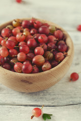 Obraz premium Red gooseberry in a bowl on wooden surface