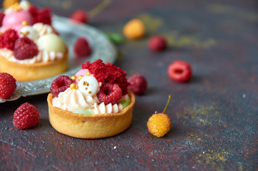 Homemade muffins with sweet cream and fresh red and yellow raspberries on a gray blurry background close up. Side view