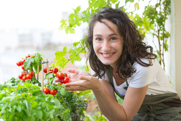 Young woman taking care of her plants and vegetables on her city balcony garden - Environment and...