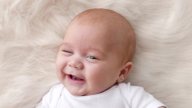 A cute little baby is looking into the camera and is happy on a white bed sheet.