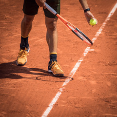 Tennis player with a ball and a rackey on a clay court at Rolland Garros