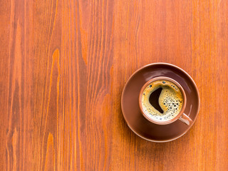 Brown cup of frothy coffee on wooden background. Top view