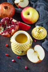 The concept of Rosh hashanah (Jewish New Year). Traditional holiday symbols - shofar, honey, apple and pomegranate on a stone or slate background. Flat lay, top view.