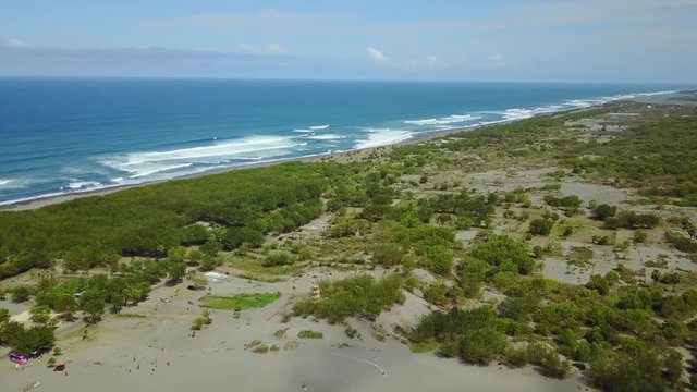 Beautiful aerial view footage of tropical coastline with trees, sand, and waves in Parangtritis, Yogyakarta, Indonesia. Shot in 4k resolution