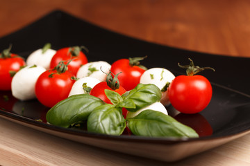 Tomatoes an mini mozarella with basil on black plate