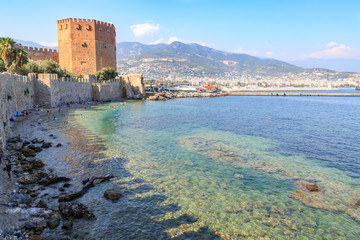 Fototapeta na wymiar Kizil (red) tower with alanya fortress with alanya city background with mountains