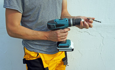 Electric screwdriver in hand of worker, drill replacement, white wall background