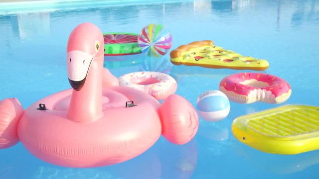 CLOSE UP: Empty inflatable flamingo, pineapple, pizza, doughnuts and watermelon floaties floating on pool water. Colorful fun pillow floats floating on water surface in empty pool