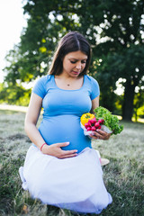Beautiful young pregnant woman holding fresh organic vegetable outdoors. Healthy lifestyle concept. 