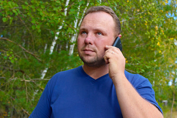 Man talking on mobile phone and looks in the upper hand on nature background. Voip, communication outside the office.