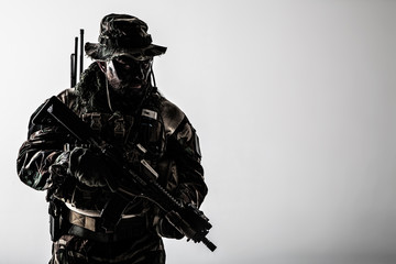 Special forces United States in Camouflage Uniforms studio shot. Holding weapons, wearing jungle hat, Shemagh scarf, painted face, he is ready to kill. Dark contrast