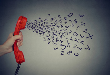 Hand holding telephone handset with alphabet letters coming out. Too many words