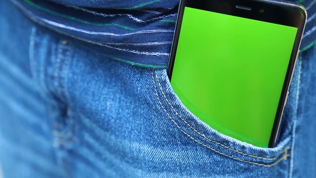 Closeup view of modern black smartphone with blank green touch screen inside of pocket of blue denim jeans. Real time full hd video footage.