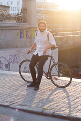 Young man posingwith the bicycle in city, hipster with leather backpack and fixie bike , sunrise background  