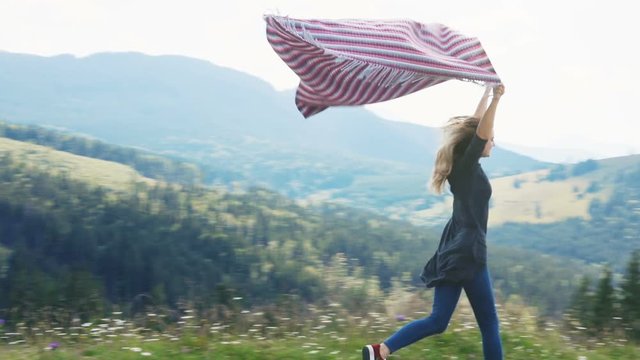 Young woman running high top mountains forest holding blanket above head wind blowing flying windy day blow summer happy wild nature freedom carefree satisfied side full view peak cheerful joying joy