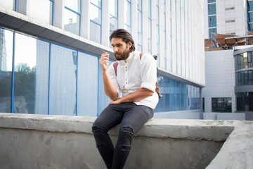 handsome guy with beard smocking cigarette on urban background with blue and gray glass  