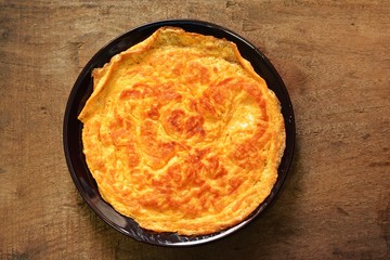 Omelet on brown plate laid on wooden floor.