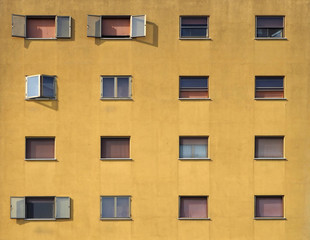 Dark yellow facade of a residential building with brown shutters. Some windows are open, others closed