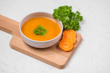 Carrot soup with cream and parsley on white stone background. Top view. Copy space