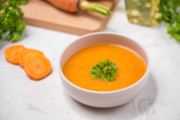 Carrot soup with cream and parsley on white stone background. Top view. Copy space