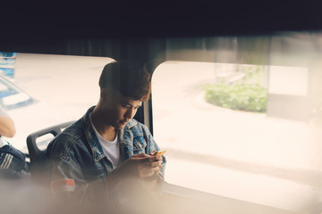Handsome asian man sitting in city bus and typing a message on the phone. © makistock