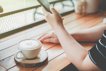 Woman using smartphone with a cup coffee in coffee shop cafe with vintage color tone filter background
