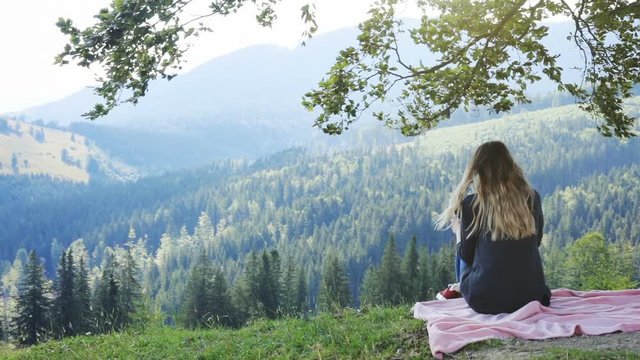Woman sitting blanket top high mountain enjoying amazing horizon wild nature beauty holding using tablet back view moving camera long hair wind blowing summer weekend leisure relaxing sunny shadow