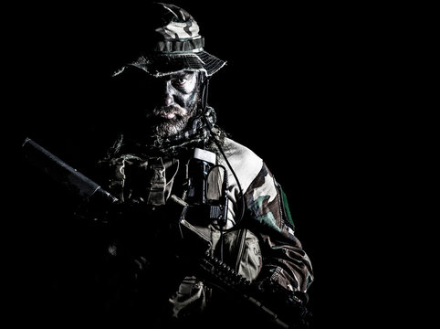 Bearded Special forces United States in Camouflage Uniforms studio shot half length black background. Holding weapons, wearing jungle hat, Shemagh scarf, he is ready to kill. Backlit