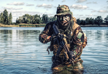 Bearded soldier of special forces in action during river raid in the jungle terrain. He is waist...