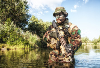 Bearded soldier of special forces in action during river raid in the jungle terrain. He is waist...