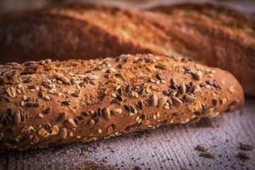 Macro view of fresh crunchy baguette bread with sunflower seeds and other seeds on the rustic wooden desk