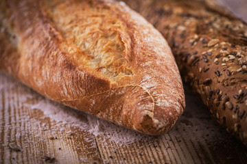 Macro view of fresh crunchy baguette bread with sunflower seeds and other seeds on the rustic wooden desk