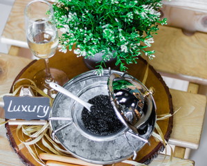 Black caviar in a silver icher with ice. Champagne is poured into the glass. Delicacy. A small slate with the inscription luxury. An exquisite gift for the holiday. Food. VIP. 