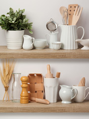 Kitchen utensils and dishware on wooden shelf.