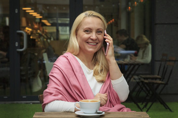 Smiling beautiful woman 45 years old drink coffee in a cafe and talking on the phone.