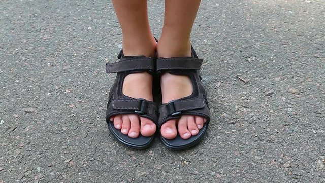 Closeup top view of feet of white child wearing brown leather sandals with black rubber soles isolated on grey urban pavement. Real time full hd video footage