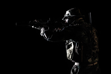 Fototapeta na wymiar Bearded Special forces United States in Camouflage Uniforms studio shot half length black background, backlit. He is shooting killing enemy, pointing the rifle