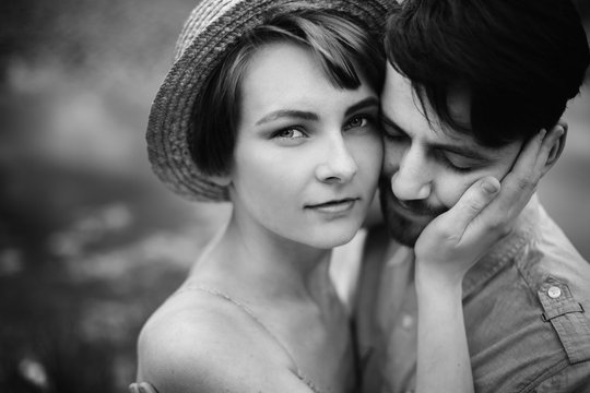 stylish hipster couple hugging at lake. man and woman embracing, in love relaxing in summer park, picnic date. girl in fashionable modern dress and straw hat . black white photo