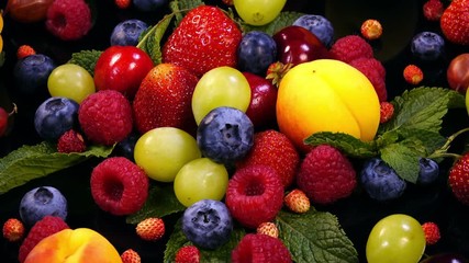 Background with mixed fresh juicy berries and fruits and mint leaves on black background in 4K. Closeup view rotation.
 - Powered by Adobe