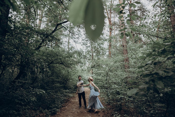 stylish hipster couple walking and dancing in green summer forest. happy man and woman in love,...