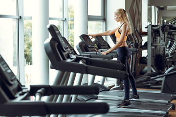 Fototapeta na wymiar athletic blond woman running on treadmill at gym.