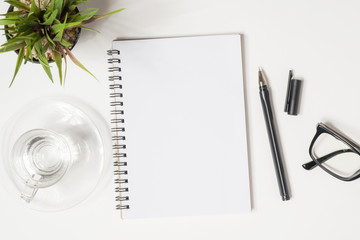 Blank notebook page is on top of white office desk table with supplies. Top view, flat lay.