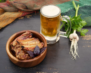 Pork fried ribs in a wooden bowl, a glass of beer and fresh greens on a table.