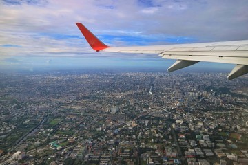 Aerial view of Bangkok, Thailand with building in big city, blue sky, white cloud and airplane's wing. View from airplane's window. Soft focus.